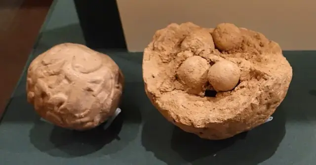 Zwei kugelförmige Tonhüllen, eine davon zerbrochen, mit kleinen Zählsteinen daneben