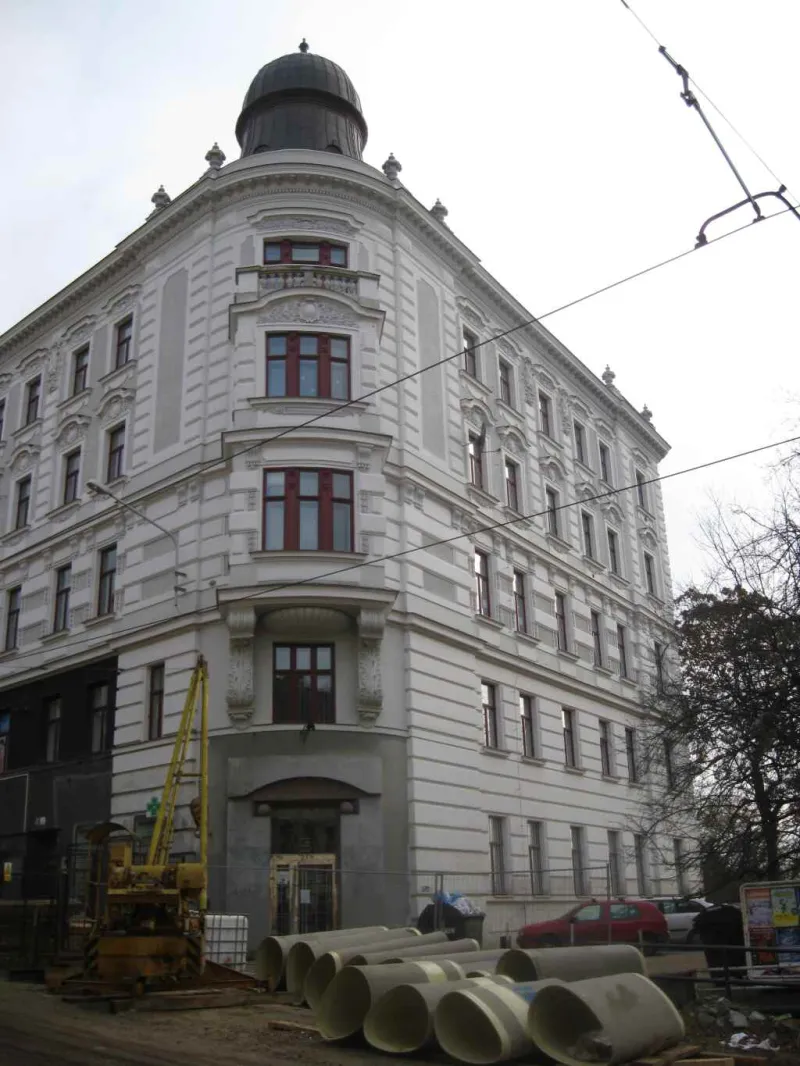 Mehrstöckiges helles Eckhaus mit Kuppel und verzierter Fassade, davor eine Baustelle mit Rohren