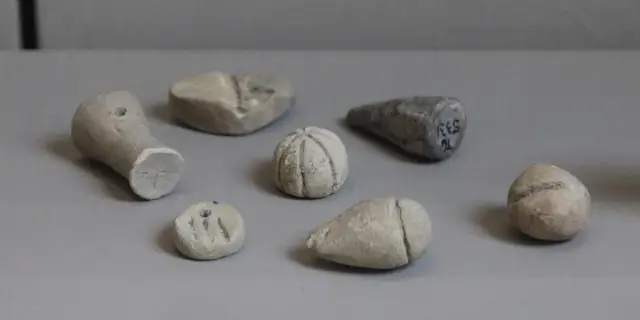 Mehrere kleine Tonobjekte in Kegel-, Kugel- und Scheibenform in einer Museumsvitrine