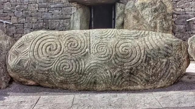 Großer, liegender Steinblock vor einem Grabeingang, bedeckt mit eingemeißelten Spiralen und Rauten