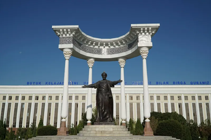 Bronzestatue von al-Chwarizmi mit ausgebreiteten Armen unter einem weißen Säulenbogen vor einem Gebäude